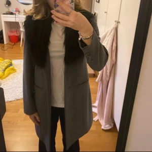 Grå kappa med svart fuskpäls - Fin grå kappa med fuskpäls, köpt på Ullared och i storleken 34. Halt oanvänd. Pris går att diskutera och jag kan skicka fler bilder💕