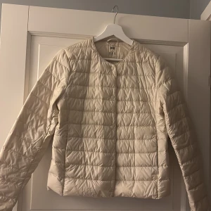 Beige dunjacka från Uniqlo - Säljer en beige, ultralätt dunjacka från Uniqlo. Jackan har en quiltad design med långa ärmar och knäppning fram. Perfekt för kyliga dagar när du vill hålla dig varm utan att känna dig tung.
