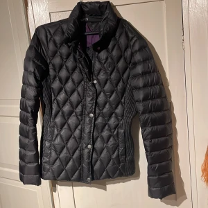 Svart quiltad jacka från Tommy Hilfiger - Snygg svart quiltad jacka från Tommy Hilfiger i storlek XS. Jackan har långa ärmar och knappar framtill. Perfekt för kyligare dagar med sin stilrena design och bekväma passform.
