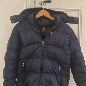 Marinblå Ralph lauren puffer jacket  - Ralph lauren puffer jacket från NK ! Skick 8-10 ! Nypris: 3000kr vårtpris: 1799kr!! Hängaren på insidan har gått.  sönder syns på bild!! Denna jacka passar bäst för 158-170cm. Mer frågor skriv till mig 