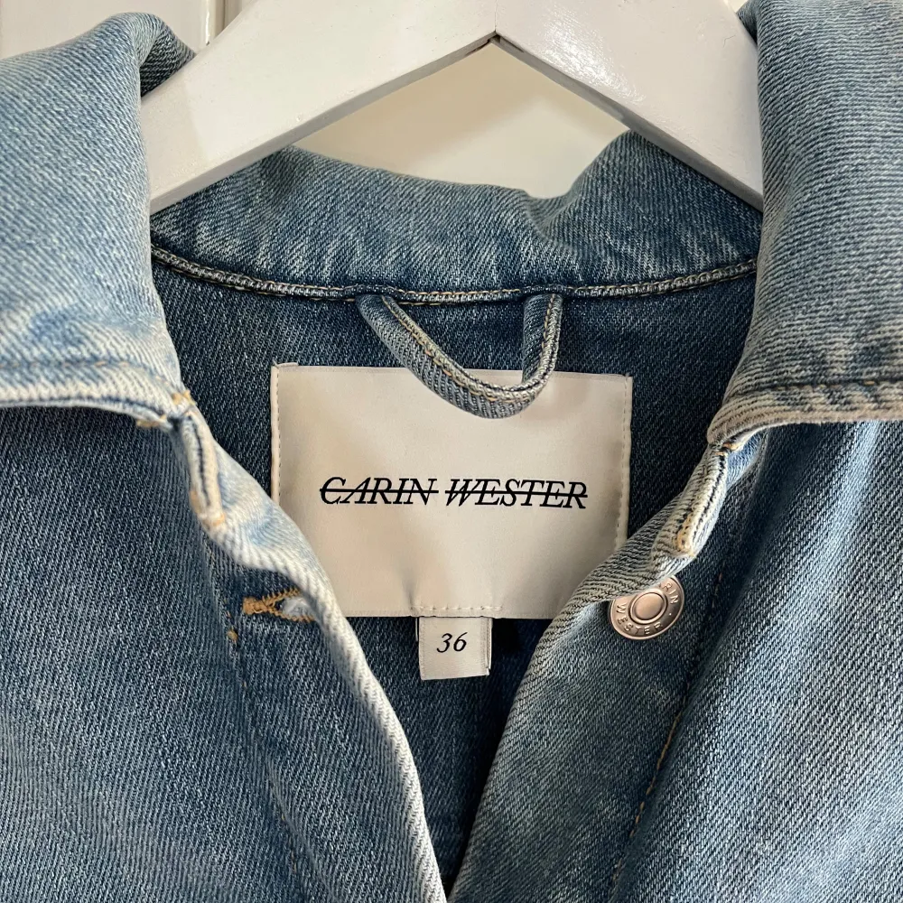 Säljer en snygg jeansjacka från Carin Wester i storlek 36. Jackan har en klassisk blå denimfärg och är utrustad med ett bälte i midjan för en mer figurnära passform. Den har långa ärmar och stora fickor framtill, perfekt för en avslappnad stil. Passar perfekt till vår och höst!. Jackor.