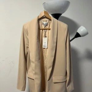 Klassisk blazer  - Den här blazern är klassisk och perfekt för arbete och har en vadderad axel. Den har långa ärmar och en rak oversized passform. 