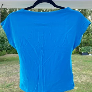 Blå topp med låg rygg - En blå t-shirt med låg rygg och tunt skönt material. Storleken är M och passar fint till mig som normalt har storlek S i toppar.  Har aldrig blivit använd så det är därför jag nu väljer att sälja den 💙😚  Längd: 47 cm Axel: 50 cm Byst: 72 cm