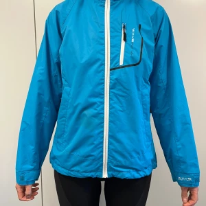 Blå vindjacka från Wave Concept - Säljer en snygg blå vindjacka från Wave Concept. Jackan har en dragkedja framtill och en praktisk bröstficka med dragkedja. Den är perfekt för blåsiga dagar och har en bekväm passform. Jackan är i storlek 38. Justerbar nedre kant. 