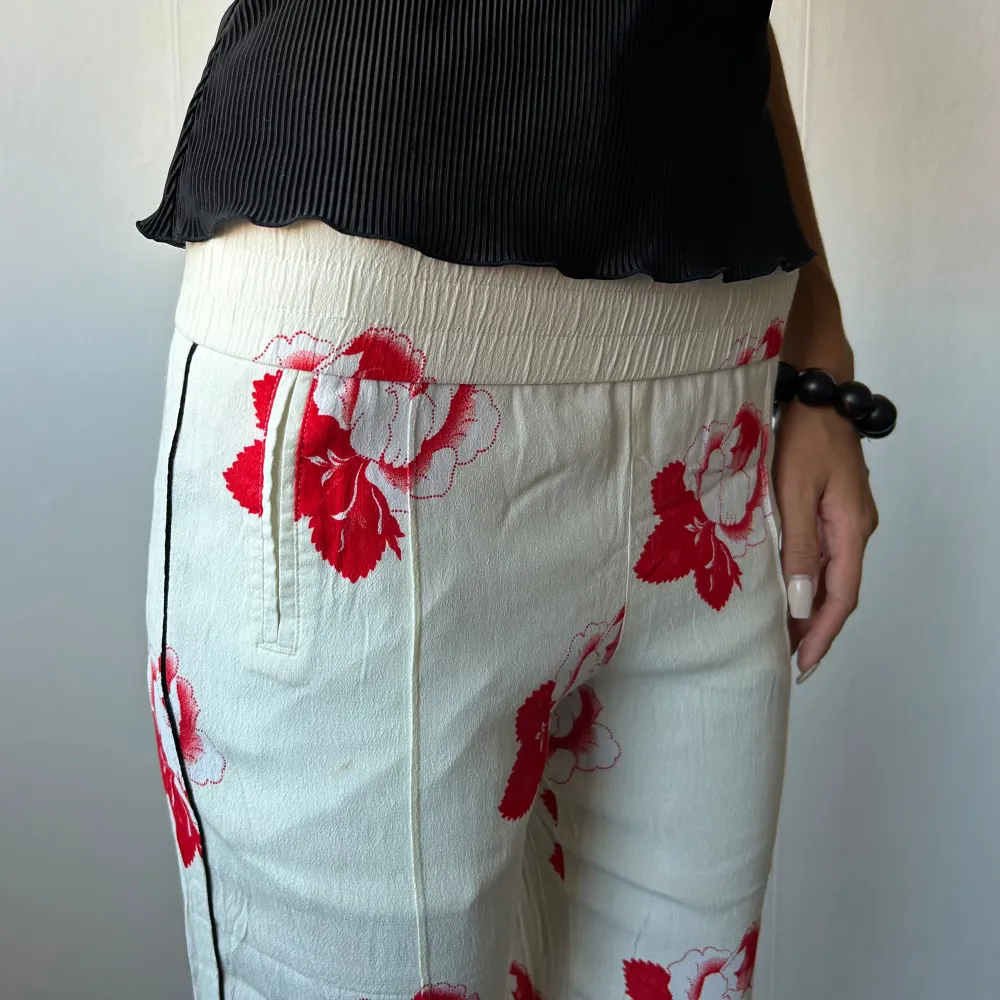 •Cream white straight leg crepe trousers with red flower print, from scandi brand Ganni. Small hole on front  • SIZE - S / EU 36 • BRAND -  Ganni • MATERIAL - 100% viscose. Jeans & Byxor.