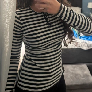 Randig långärmad tröja med snörning - Säljer en superfin randig tröja i svart och vit med långärmade ärmar. Den har en snygg snörning framtill som ger en extra detalj. Perfekt för  vardag och finare tillfällen!