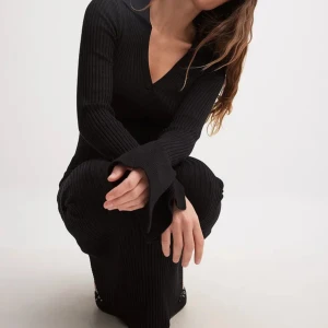 Ribbstickad klänning från NA-KD - Den här svarta maxiklänningen har en åtsittande passform och en stretchig ribbstickning. Den har en piké krage och långa trumpetärmar med utskuren detalj. Beställde två storlekar men behåller 1. Nyskick 