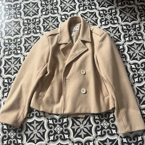 Kappa NA-KD - Beige kappa med vita stora knappar från NA-KD. Väldigt fint skick. Hel och ren. Inga defekter. Nypris(köpt för): 799 kr