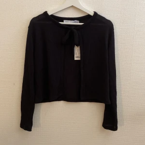 Svart stickad kofta från 157 - Säljer en snygg svart kofta från Lager 157 i storlek XS. Den har långa ärmar och en knytning framtill som ger en fin detalj. Perfekt för höst och vinter när du vill hålla dig varm och stilren. Koftan är i nyskick och redo för en ny garderob!