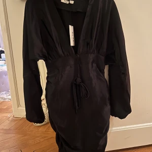 Svart satinklänning - Svart, kort satinklänning som är helt oanvänd+ lapp kvar. En åtsittande passform på nedre delen av klänningen. Riktig snygg!! i storlek xs men kan även passa S