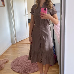 Beige klänning  - Säljer en superfin beige klänning. Den har korta ärmar och knappar hela vägen ner. Klänningen är i ett lätt och luftigt material, perfekt för varma dagar. Den har också fina spetsdetaljer som ger en romantisk touch. Passar perfekt till sommarens alla fester eller en avslappnad dag på stan.