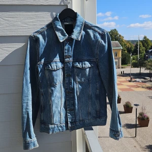 Jeansjacka från J.Lindeberg - Säljer en snygg jeansjacka från J.Lindeberg i storlek S. Jackan är i klassisk blå denim med knappar framtill och två bröstfickor som går att stänga. Perfekt för vår och höst, och ger en cool och avslappnad stil. Tillverkad i Turkiet.