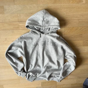 Grå hoodie med text - Säljer en grå hoodie med texten 'MA CHÉRIE' i glittriga detaljer på framsidan. Tröjan har en klassisk huva med dragsko och långa ärmar. Perfekt för en avslappnad stil.