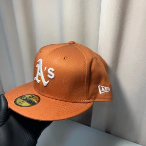 New Era keps - Snygg orange keps från New Era med broderad vit logga på framsidan. Kepsen har en klassisk 59FIFTY design med en platt skärm och broderad MLB-logga på baksidan. Perfekt för att ge din outfit en sportig touch.