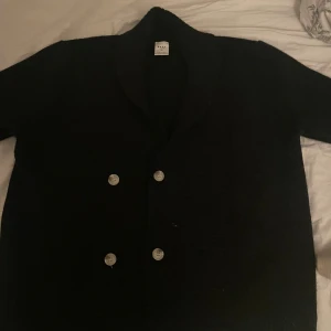 Svart stickad tröja - Snygg stickad dubbelknäppning och klassisk krage. Perfekt för en stilren look. Passar bra till både vardag och mer formella tillfällen.