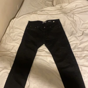 Svarta jeansbyxor - Snygga svarta jeansbyxor med klassisk design. De har en rak passform och är perfekta för en stilren look. Byxorna har fickor både fram och bak samt knappar i midjan.