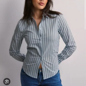Randig skjorta från Nelly - Snygg randig skjorta från Nelly i ljusblått med svarta ränder. Skjortan har långa ärmar och knappar framtill. Perfekt för en stilren look.