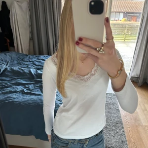 Vit långärmad topp med spetsdetaljer - Säljer en stilren vit långärmad topp med vacker spetsdetalj vid halsringningen. Den är nästan helt oanvänd och mycket fin💕