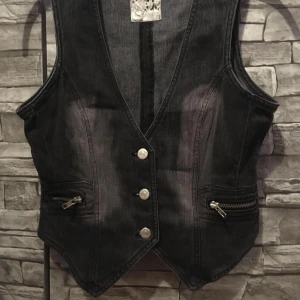 Snygg jeansväst i storlek 170 - Snygg jeansväst från Detroit med v-ringning och knappar framtill. Västen har dragkedjefickor och justerbar rem  baktill Perfekt för en cool och avslappnad stil.
