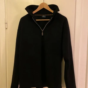 Svart tröja med dragkedja från Sand Men - Snygg svart tröja från Sand Men med dragkedja i halsen. Perfekt för en stilren look. Tröjan har långa ärmar och en hög krage som ger extra värme. Passar bra till både vardag och mer uppklädda tillfällen.