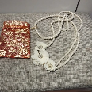 Vitt pärlhalsband med blommor - Elegant vitt pärlhalsband med flera rader av pärlor och vackra vita blommor med glittriga detaljer. Perfekt för att ge en sofistikerad touch till din outfit. Halsbandet har en justerbar kedja för perfekt passform. Längd 50 cm.