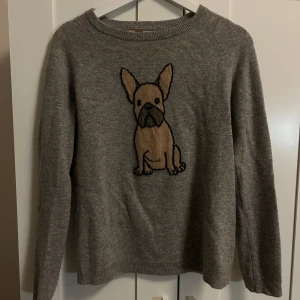 Grå stickad tröja med hundmotiv - 100% cashmere!! Säljer en mysig grå stickad tröja med ett charmigt hundmotiv på framsidan. Tröjan har långa ärmar och en rund halsringning. Perfekt för hundälskare som vill ha något unikt i garderoben. 🐶