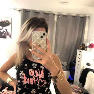 Svart linne med tryck - Snyggt svart linne med rosa texten 'New York' och vita palmträd. Perfekt för en avslappnad stil. Linnet har en bekväm passform och ärmlös design.