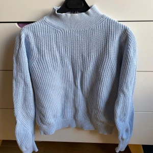 Ljusblå stickad tröja från Esprit - Säljer en ljusblå stickad tröja från Esprit. Tröjan har en hög krage och långa ärmar med ribbade muddar. Perfekt för kyligare dagar och ger en stilren look. Passar bra till både jeans och kjol.