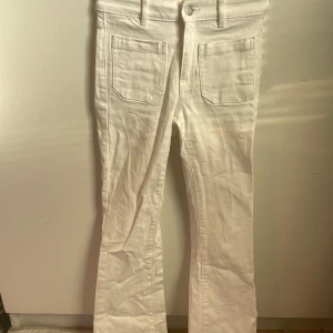 Vita bootcut byxor Winnie - Snygga vita bootcut byxor i modellen Winnie. De har en klassisk design med fram- och bakfickor samt hällor för bälte. Perfekta för en stilren look.