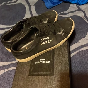 Svarta sneakers från Saint Laurent - Snygga svarta sneakers från Saint Laurent med vit sula och snörning. Skorna har en stilren design med märkets logga på sidan. Perfekta för en trendig look.