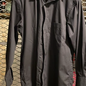 Svart skjorta från A.W. Dunmore - Snygg svart skjorta från A.W. Dunmore med klassisk krage och knappar framtill. Skjortan har en bröstficka och är tillverkad i ett strykfritt material, perfekt för en stilren look utan krångel.