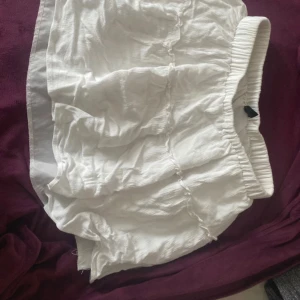 Vit kjol med resårmidja - Säljer en vit kjol med resårmidja. De har en avslappnad passform och är perfekta för varma dagar. Materialet ser ut att vara lätt och luftigt, vilket gör dem bekväma att bära.