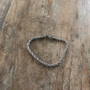 Flätat silverarmband - Snyggt flätat armband i silverfärg med en enkel och stilren design. Perfekt för att lägga till en elegant touch till din outfit. Armbandet har en säker låsning som håller det på plats. Den är 20 cm lålg 