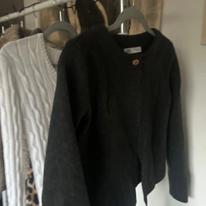 Mörkgrå kofta från Zara - Säljer en stilren mörkgrå kofta från Zara med en enkel knapp framtill. Perfekt för kyligare dagar och lätt att matcha med olika outfits. Koftan har långa ärmar och en rund halsringning.