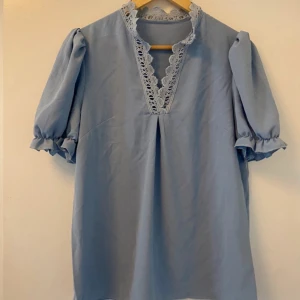 Ljusblå blus med spetsdetaljer - Charmig ljusblå blus med v-ringad spetsdetalj och puffiga kortärmar. Perfekt för en somrig look med sin luftiga design och romantiska touch. 💙