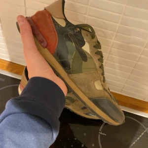 Valentino Rockrunner i camouflage - Säljer ett par Valentino Rockrunner sneakers i camouflage. Skorna har en unik kombination av gröna, bruna och röda nyanser med snörning och en robust sula. Perfekta för dig som vill ha en stilren och trendig look.