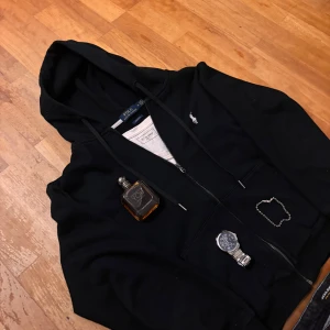 Ralph Lauren zip - Säljer en stilren svart hoodie med dragkedja och en liten broderad logga på bröstet. Perfekt för en avslappnad look. Passar bra till jeans eller träningsbyxor.