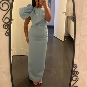 Ljusblå långklänning med stor rosett - Super fin ljusblå med en stor rosett på ena axeln. Endast använd några timmar under en kväll. Stl 40, men är mer som en 38 & jag är 160  🩵  Köpt för 3899 kr