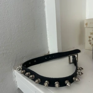 Svart nitat bälte - Coolt svart bälte med silverfärgade nitar. Perfekt för att ge en edgy touch till din outfit. Justerbar storlek med flera hål för bästa passform.