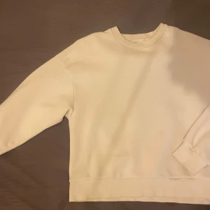 Vit sweatshirt - Säljer en klassisk vit sweatshirt med rund hals och långa ärmar. Perfekt för en avslappnad stil. Tröjan har ribbade muddar vid ärmslut och nederkant.