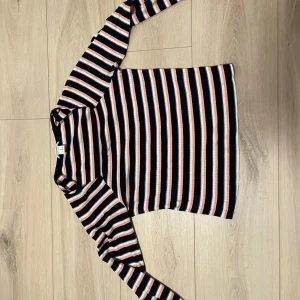 Randig långärmad tröja från Monki - Säljer en randig långärmad tröja från Monki i svart, vit och orange. Tröjan har en klassisk passform och är perfekt för både vardag och avslappnade tillfällen. Den är tillverkad i ett mjukt och bekvämt material.