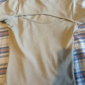 Beige ribbad topp - Säljer en stilren beige ribbad topp med korta ärmar. Toppen har en unik design med en öppen detalj framtill. Perfekt för en trendig look!