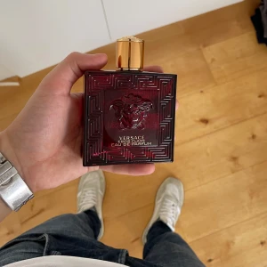 Versace Eros Flame Eau de Parfum - Säljer en elegant Versace Eros Flame Eau de Parfum. Flaskan är fyrkantig och djupröd med ett guldigt lock. Den har ett stilrent mönster och den ikoniska Medusa-loggan på framsidan. Perfekt för den som vill ha en lyxig doftupplevelse. Ungefär 40% kvar