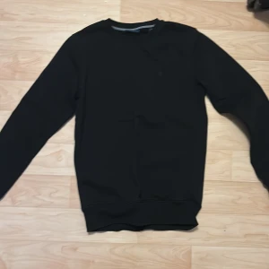 Svart tröja från Gant - Säljer en stilren svart tröja från Gant. Tröjan har långa ärmar och en rund halsringning med ribbade kanter. Perfekt för en avslappnad och snygg look. Passar bra till både jeans och chinos.