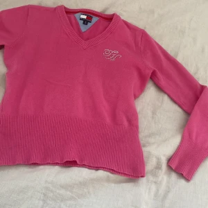 Rosa tröja från Tommy Hilfiger - Säljer en snygg rosa tröja från Tommy.Tröjan har en v-ringad hals och är croppad med långa ärmar. Den ser mindre ut än vad den är! 
