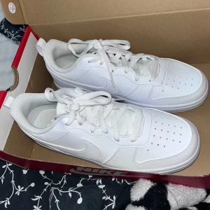 Vita sneakers från Nike - Säljer ett par stilrena vita sneakers från Nike. Skorna har klassisk snörning och en diskret Nike-logga på sidan. Perfekta för en clean look.