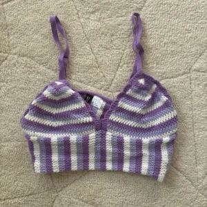 Lila och vit randig linnetopp - Säljer en söt lila och vit randig linnetopp med smala axelband. Toppen har en v-ringad design och är croppad och är perfekt för varma dagar. Den är stickad och ger en skön och luftig känsla. Passar bra till både jeans och kjol.