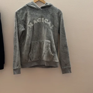 Grå hoodie med texten 'MAGICAL' - Mysig grå hoodie med texten 'MAGICAL' på framsidan. Tröjan har en stor ficka framtill och en huva med ett sött djuransikte och öron. Perfekt för en avslappnad och bekväm stil. är i storlek 158/164