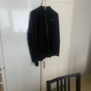Nike  - Säljer en svart jacka med dragkedja och hög krage. Jackan har långa ärmar och en enkel design som passar till många tillfällen. Perfekt för kyligare dagar.