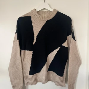 Beige och svart stickad tröja - Säljer en snygg stickad tröja i beige och svart med ett unikt geometriskt mönster. Tröjan har långa ärmar och en rund halsringning. Perfekt för att hålla sig varm och stilren under kyligare dagar. Sitter som S dam.